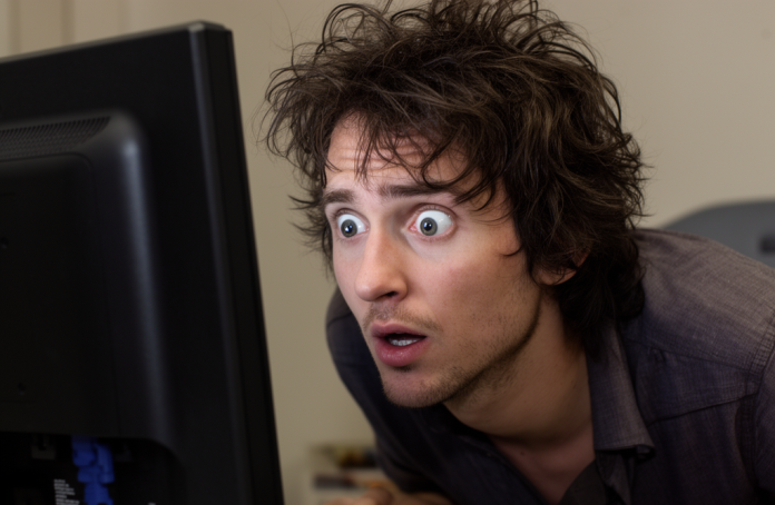 Программист с взъерошенными волосами смотрит выпученными глазами в монитор компьютера